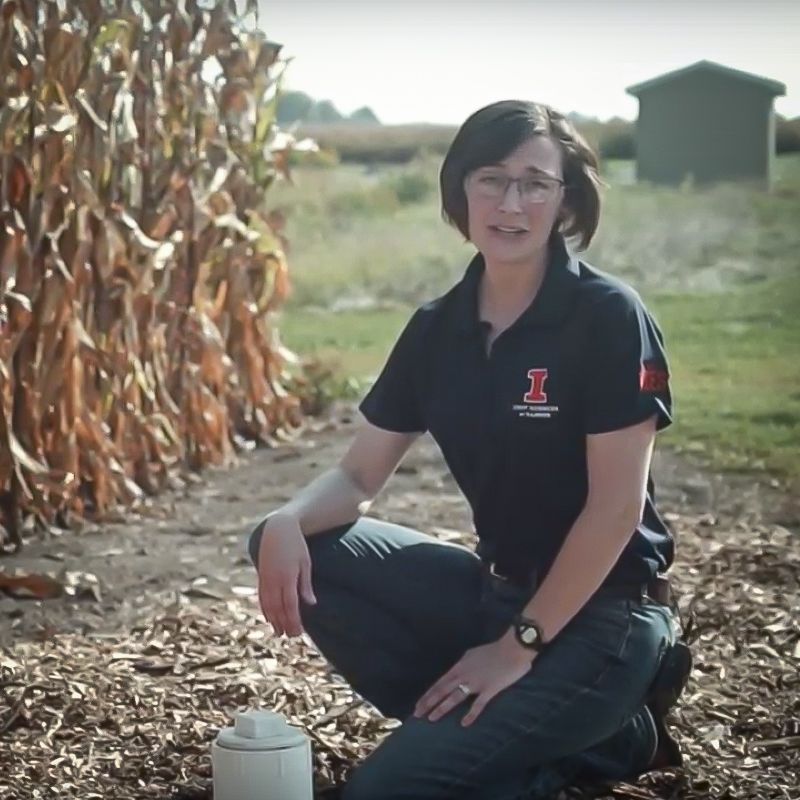 Laura kneeling near cornfield.