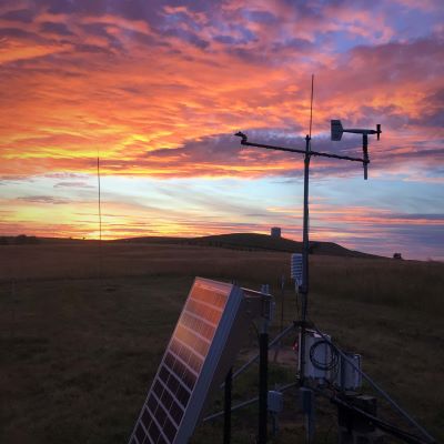 a solor panel and weather station in front of sunset