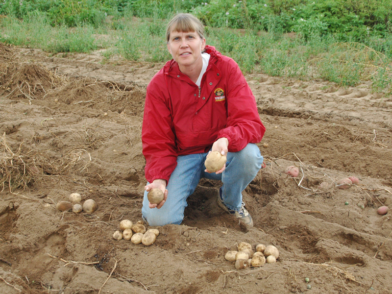 Shelly kneeling next to potatoes on soil.