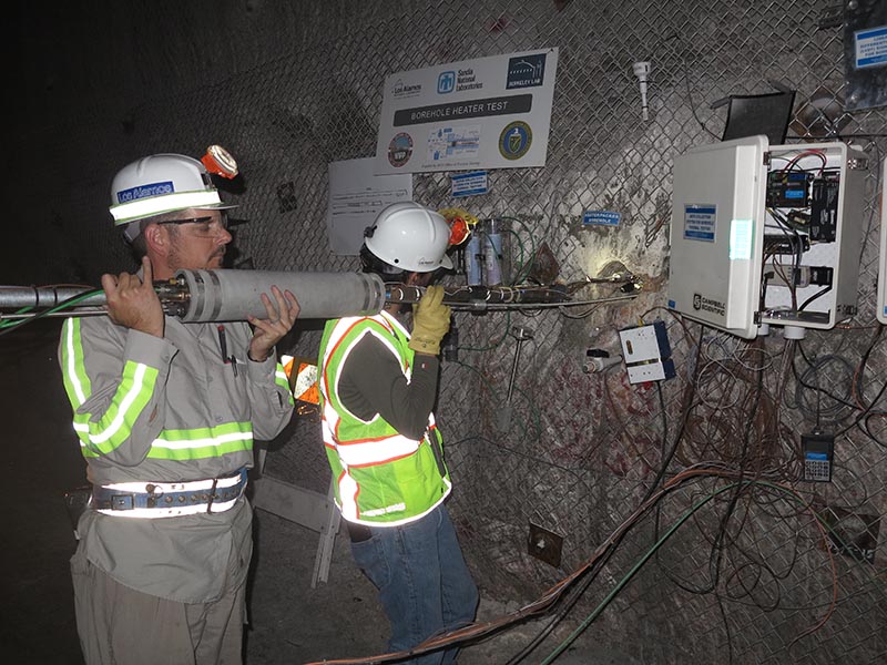 Two men placing heater into bored hole.