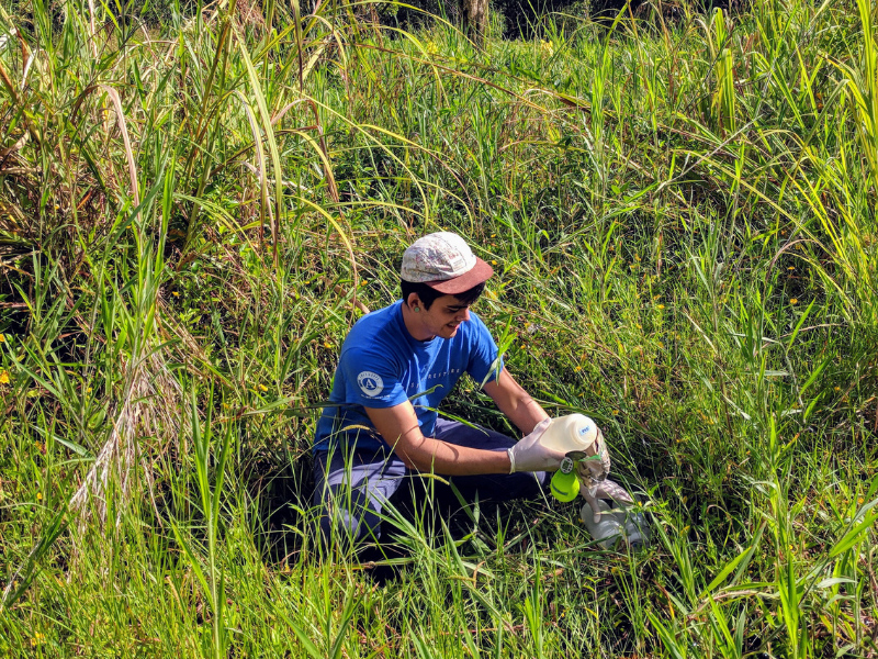 man wearing hat kneeling in tall grass using equipment