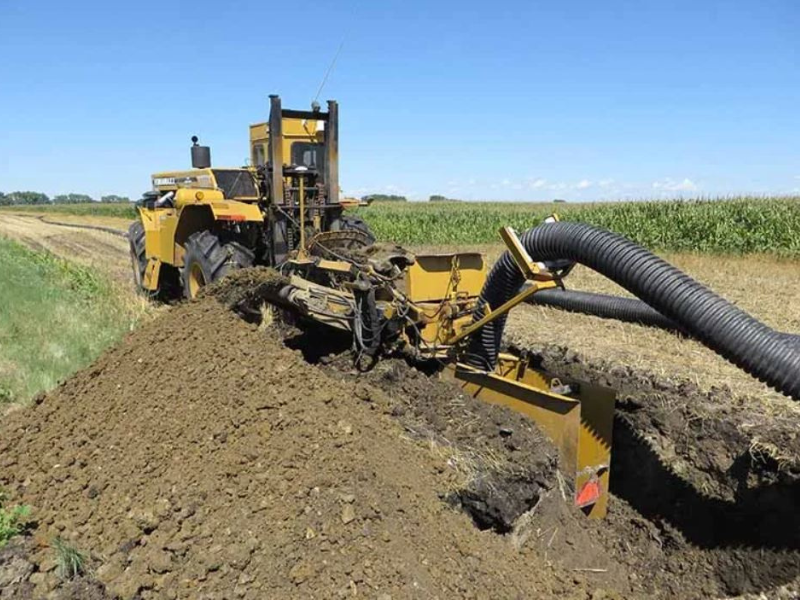 tractor installing drain tile in farm field