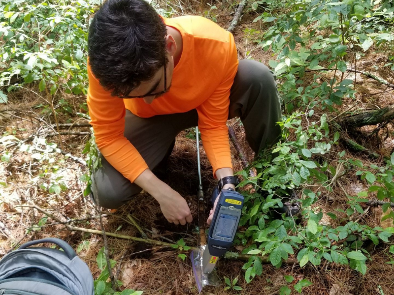 male scientist kneeling on old orchard ground using soil probe and equipment